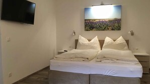 A bedroom with a bed, a flat-screen TV mounted on the wall, and a painting above the bed. - Holiday apartment with infrared (Rauris)