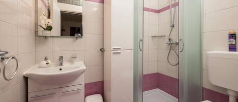 Moderni kylpyhuone, jossa on lasiseinällä varustettu suihku, valkoinen pesuallas ja wc.
