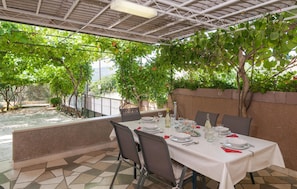 An outdoor dining area with a table set for four, surrounded by greenery and a view of a water feature.