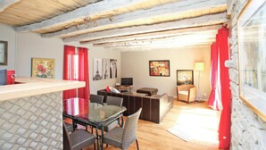 A cozy living room with a glass-top dining table, wicker chairs, a brown sofa, a TV, and red curtains. - Stunning home in Coly with WiFi (Coly)