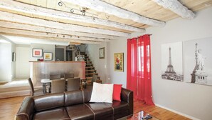 A living room with a brown leather sofa, a glass coffee table, and red curtains. There is a staircase leading to an upper level, and two framed pictures on the wall. - Stunning home in Coly with WiFi (Coly)