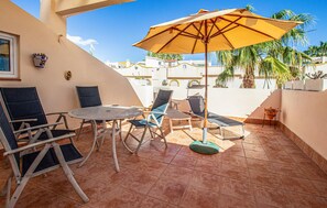 Een terras met een ronde tafel, vier stoelen, een parasol en potplanten.