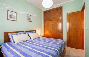 Een slaapkamer met een bed, twee ingelijste foto’s aan de muur, een houten kledingkast en een deur.