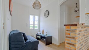 Ein Wohnzimmer mit blauem Sofa, einem kleinen Tisch mit Dekoration, einer Wanduhr und einer Wand aus Ziegelsteinen.