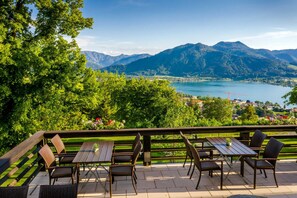 An outdoor patio with a wooden table and chairs, overlooking a lake and mountains.