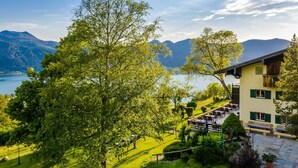 Eine Berghütte mit einer Terrasse mit Blick auf einen See, umgeben von üppiger Vegetation und Bergen.