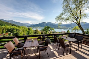 Une terrasse extérieure avec des tables et des chaises, offrant une vue sur un lac et des montagnes.