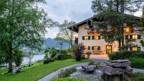 Ein mehrstöckiges Gebäude mit Balkon, umgeben von Grün und mit Seeblick.