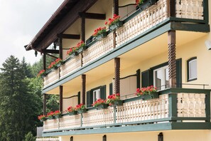 Ein mehrgeschossiges GebĂ€ude mit Balkonen, die mit roten Blumen, Holzbalken und traditioneller Architektur geschmĂŒckt sind.