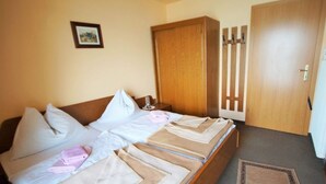 A double bed with two pillows, a bedside table, a wooden wardrobe, and a door with a handle.