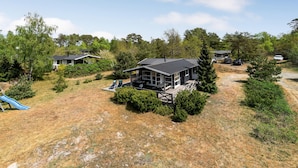 Een modern huis met een ruim terras, omgeven door een droog grasveld en dichte bomen.
