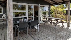 Een terras buiten met een tafel en stoelen, een houten terras en een overdekt gedeelte met ramen.
