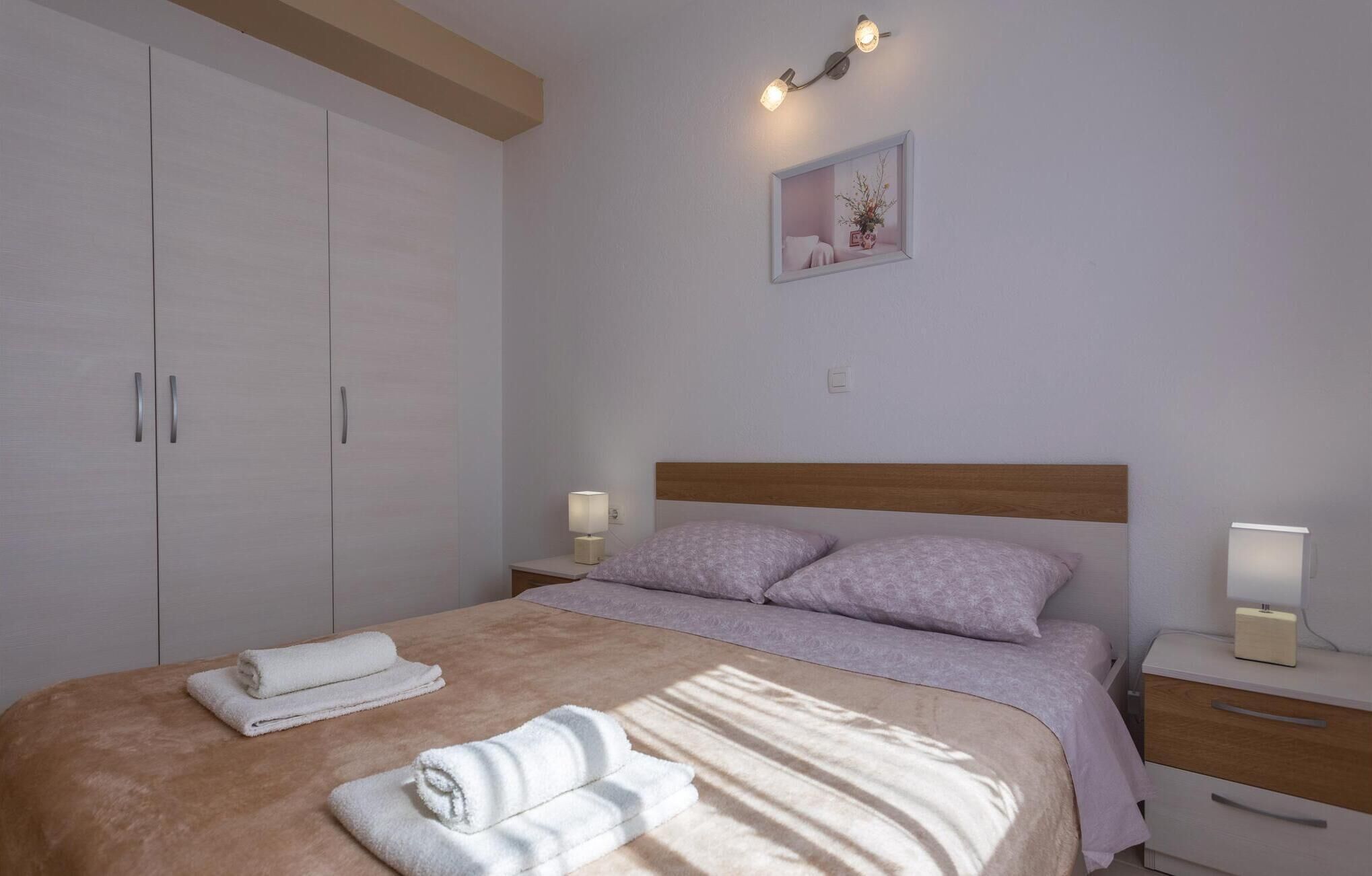 A bedroom with a bed, two bedside tables with lamps, a nightstand, a wardrobe, and a framed picture on the wall.