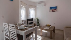 A dining area with a white table set for two, a potted plant, and a painting on the wall.