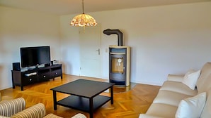 A living room with a sofa, a striped chair, a coffee table, a TV, and a wood-burning stove. - Apartment 2 - large apartments in the Manor House (Weitendorf)