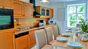 A kitchen with wooden cabinets, a dishwasher, a stove, and a dining area with striped chairs and a table set for a meal. - Apartment 2 - large apartments in the Manor House (Weitendorf)