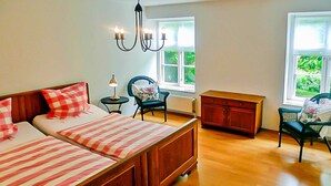 A bedroom with a large bed, a nightstand, a chair, a dresser, and a window with a view of greenery. - Apartment 2 - large apartments in the Manor House (Weitendorf)