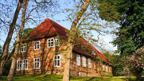 A large, traditional stone building with a red-tiled roof, surrounded by lush greenery and trees. - Apartment 2 - large apartments in the Manor House (Weitendorf)