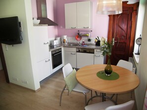 A compact kitchen with white cabinets, a stove, a dishwasher, and a dining area with a table and chairs.