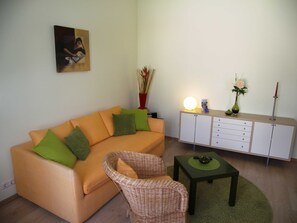 A living room with a sofa, a wicker chair, a small table, a cabinet, and a vase with flowers.