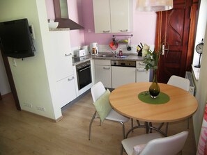 A compact kitchen with white cabinets, a built-in oven, a coffee maker, and a dining table with chairs.