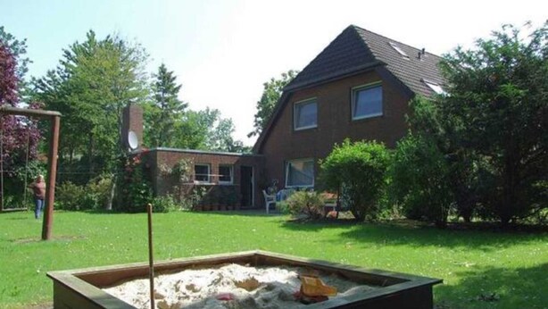 Et hus med en baghave, hvor der er en sandkasse og et gyngestativ.