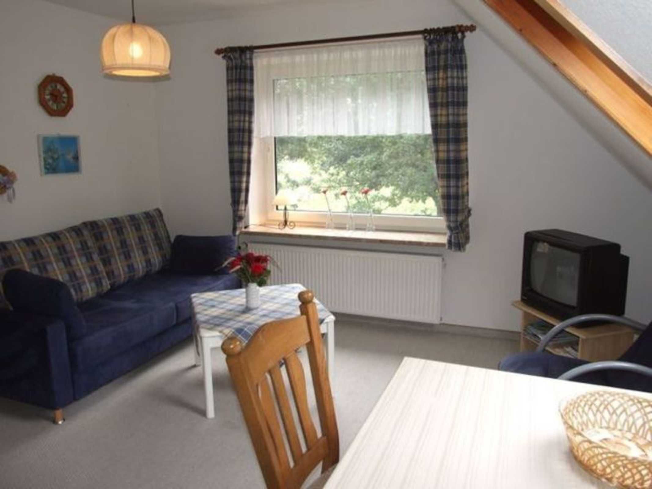 A cozy living room with a sofa, a small table, a chair, a television, and a window with curtains.
