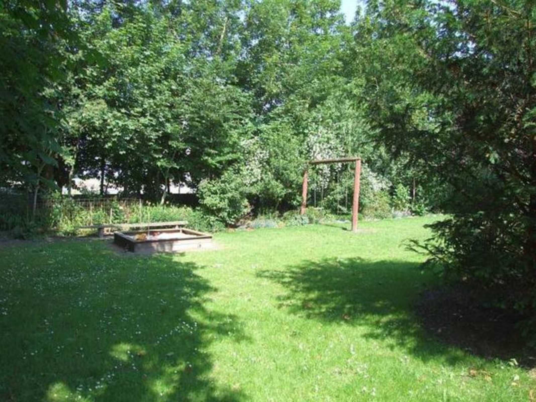 A grassy outdoor area with a wooden swing set and a concrete structure, surrounded by trees.