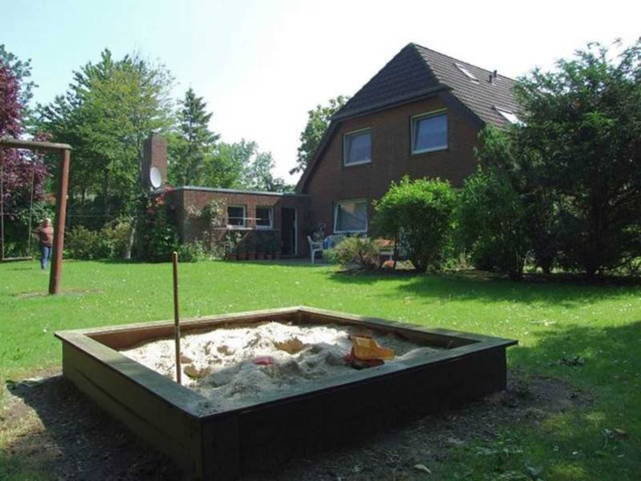 Une maison avec un jardin qui comprend un bac à sable et une balançoire.