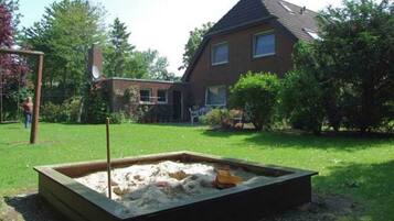 A house with a backyard containing a sandbox and a swing set.