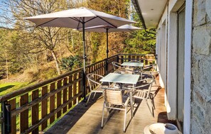 Eine Holzterrasse mit Gartenmöbeln, darunter Tische und Stühle, und einem großen Sonnenschirm.