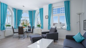 A modern living room with a dining area, large windows with curtains, and a view of the outside.