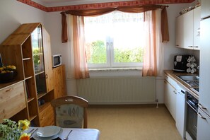 A compact kitchen with a dining area, wooden cabinets, a radiator, and a window with curtains.