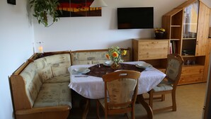 Een eetruimte met een houten tafel gedekt voor vier personen, een gestoffeerde bank en een houten kast met glazen deuren.