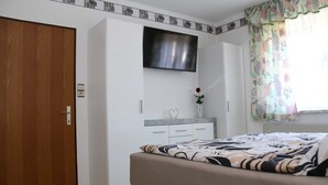 Een slaapkamer met een bed, een aan de muur bevestigde televisie, een kledingkast en een raam met gordijnen.
