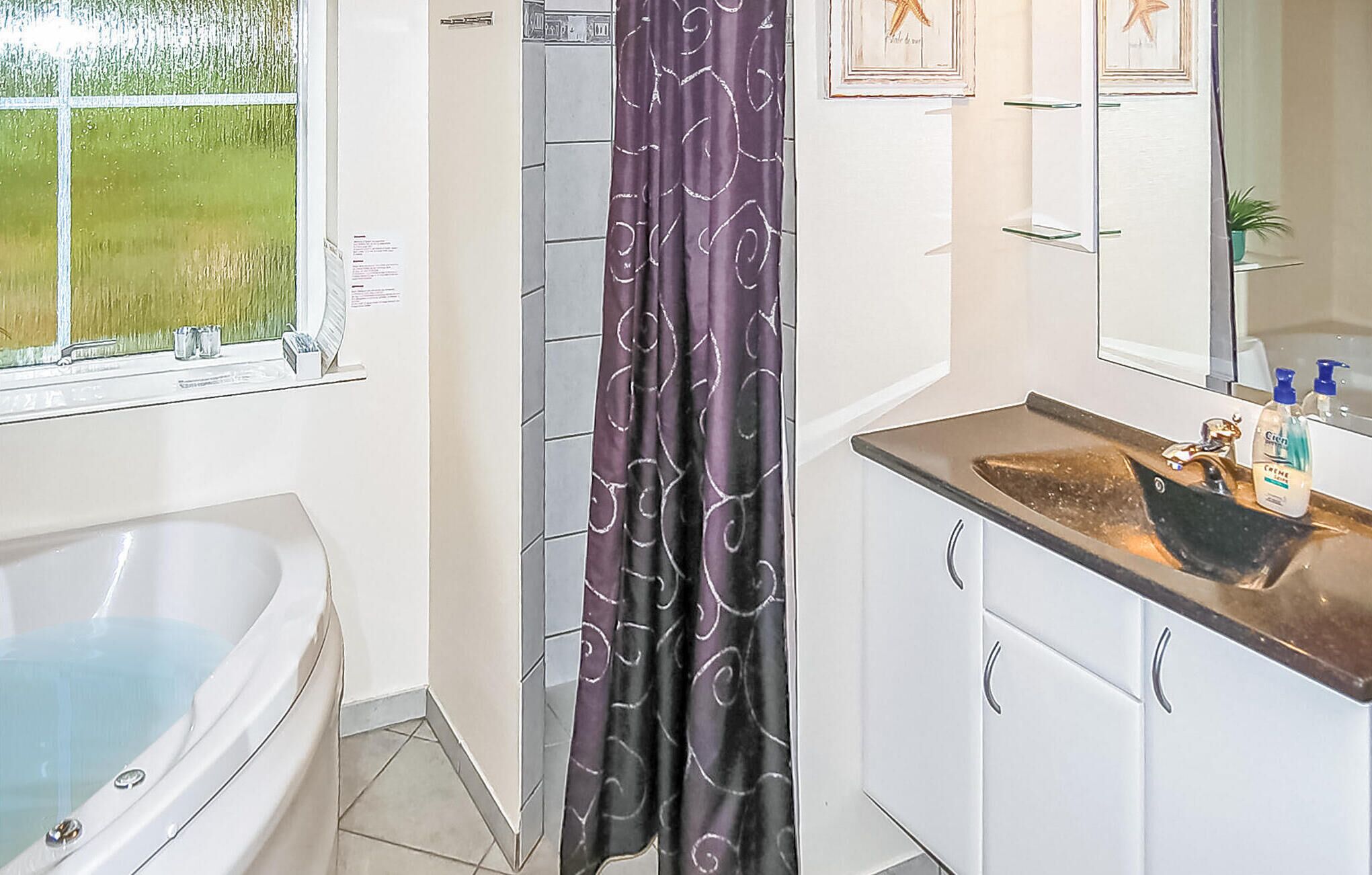 A bathroom with a bathtub, a shower curtain, a sink with toiletries, and a mirror.
