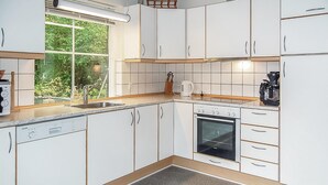 A modern kitchen with white cabinets, a built-in dishwasher, a stove, and a window with a view of greenery.