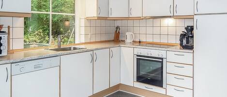 Eine moderne Küche mit weißen Schränken, einem eingebauten Geschirrspüler, einem Herd und einem Fenster mit Blick auf Grünflächen.