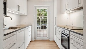 A modern kitchen with white cabinets, a wooden ceiling, and a view of outdoor furniture through a glass door. - Gorgeous home in Rømø with sauna (Rømø)