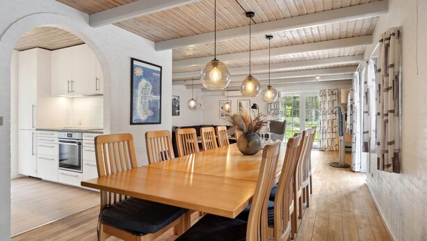 A spacious dining area with a wooden table and chairs, a kitchen in the background, and pendant lighting. - Gorgeous home in Rømø with sauna (Rømø)