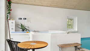 A spa area with a wooden table, black chairs, a white bathtub, and a window overlooking a pool. - Gorgeous home in Rømø with sauna (Rømø)