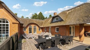 A thatched-roof building with a wooden deck, lounge chairs, and a table with chairs. - Gorgeous home in Rømø with sauna (Rømø)