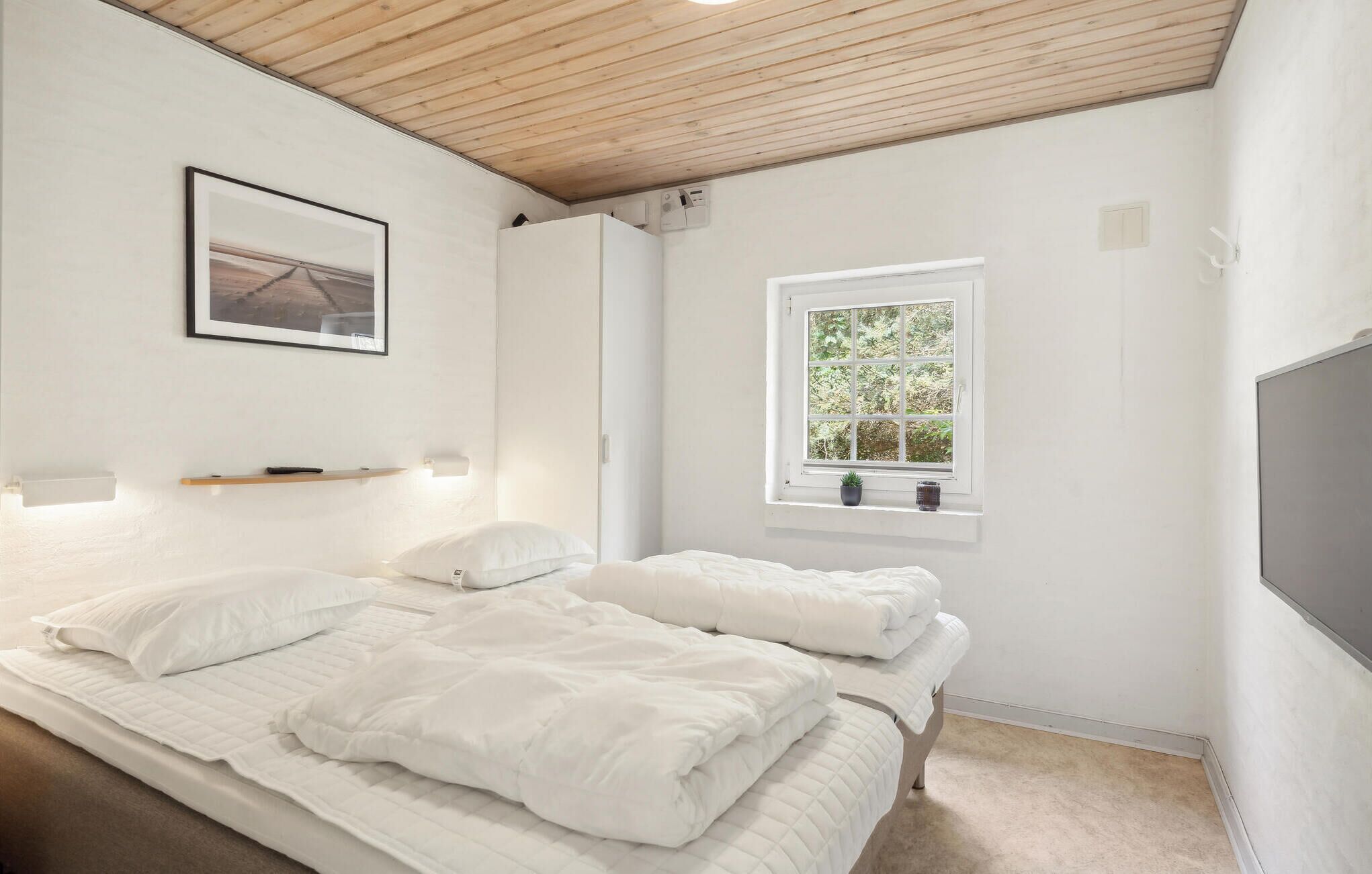 Un dormitorio con una cama, una ventana que ofrece vistas a zonas verdes, un cuadro enmarcado en la pared y una estantería con una lámpara.