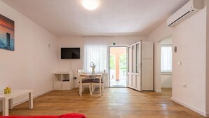 Ein Zimmer mit einem Bett, einem Schreibtisch, einem Stuhl, einem Fernseher und einer Tür zu einem Außenbereich.