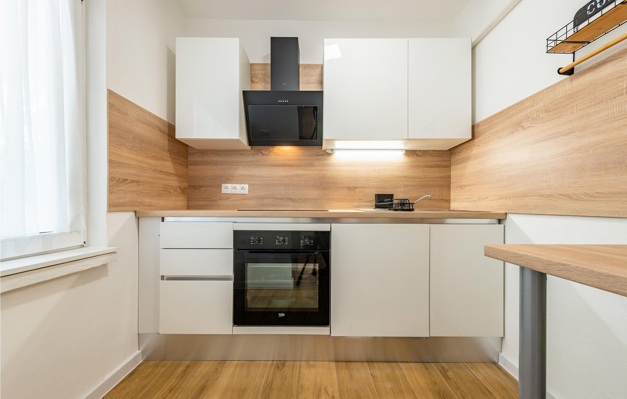 A compact kitchen with white cabinets, a black oven, and a wooden backsplash.