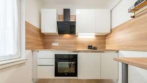 Eine kompakte Küche mit weißen Schränken, einem schwarzen Backofen und einer Holzrückwand.
