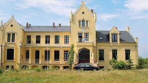 A large, yellow building with a central tower, multiple windows, and a car parked in front. - Beautiful home in Schwasdorf with sauna (Schwasdorf)