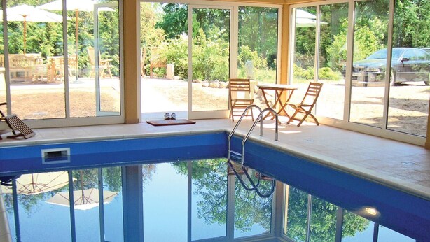 An indoor swimming pool with clear glass walls, wooden deck chairs, and a view of the outdoors. - Beautiful home in Schwasdorf with sauna (Schwasdorf)