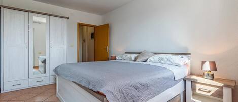 A bedroom with a bed, bedside table, lamp, wardrobe, and an air conditioning unit.
