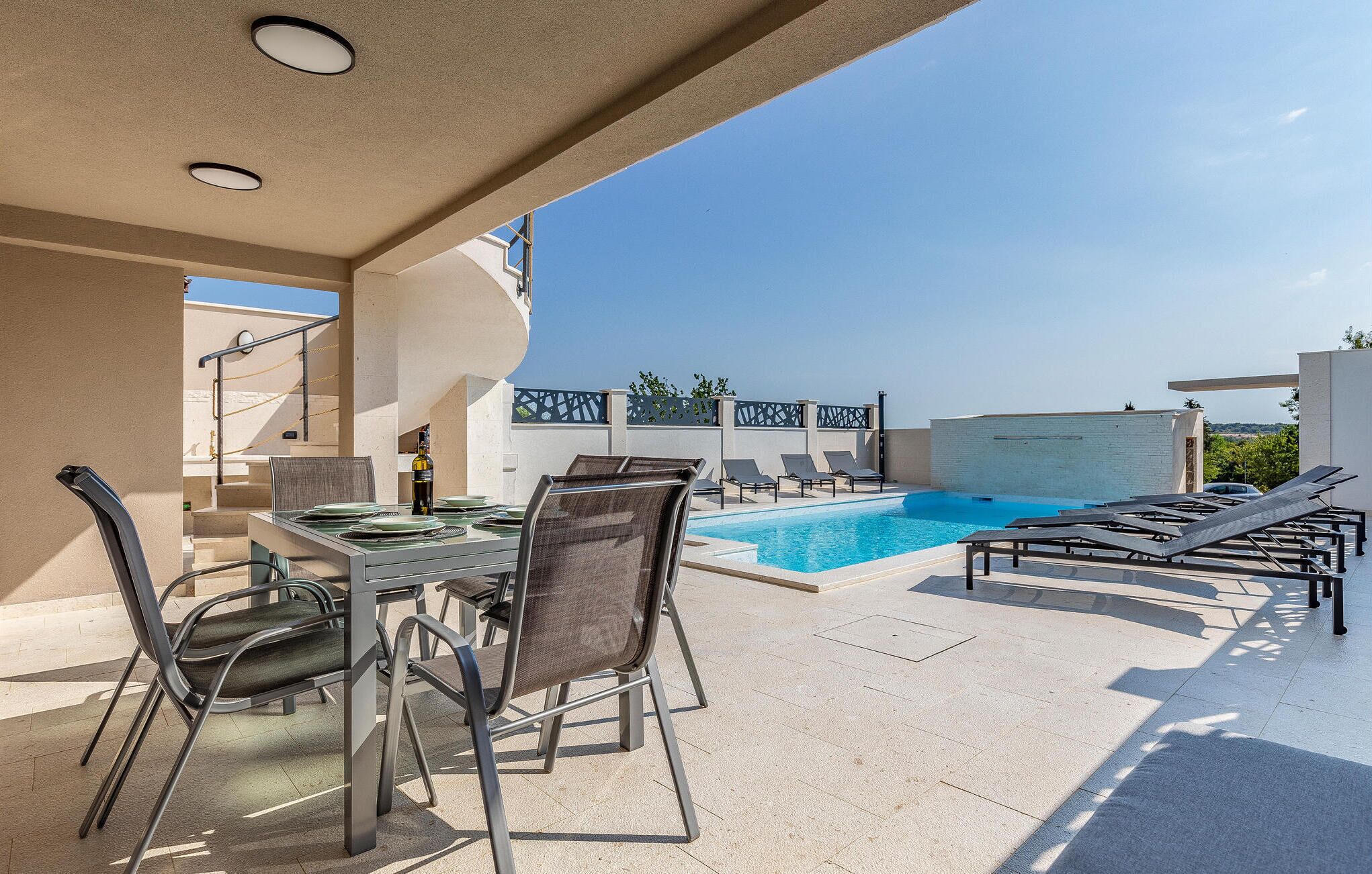 A rooftop pool area with a table and chairs, lounge chairs, and a clear view of the sky.